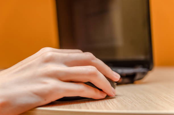 Female hand with a mouse on a wooden table next to a laptop
