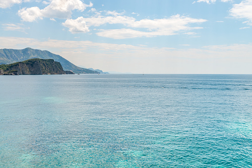 Calm sea surface with island and distant mountains silhouettes on the horizon