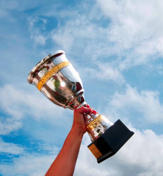 The winner takes it all. Champion winner trophy cup on sky background. First price to winner, cup trophy in silver and gold. Hand holding it up with cloudy but blue sky. Copy space in top and to left. competition heat stock pictures, royalty-free photos & images