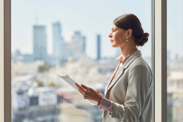 istock Attractive businesswoman holding a document folder standing near window in office. 1256315935