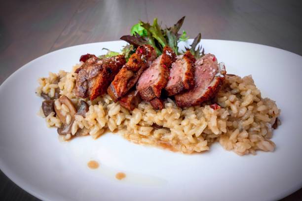 Luxury roasted duck breast on mushroom risotto on white plate, closeup.