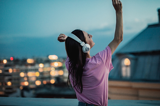Young woman with headphones dancing on the rooftop