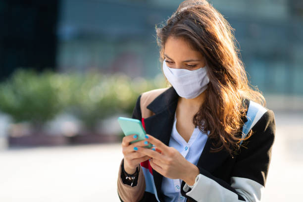 istock Woman with protective mask using mobile phone outdoors 1256318617