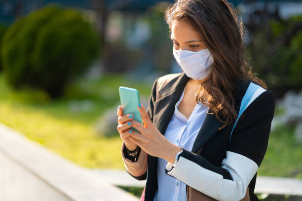 istock Woman with protective mask texting outdoors 1256318623