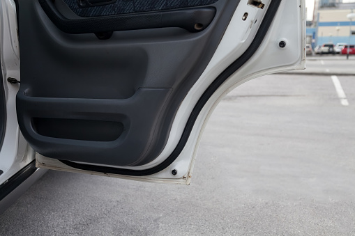 Close-up open door of a white car with a black panel in the interior finished with fabric after dry cleaning in a car service against the background of a parking lot and a manhole on the asphalt.