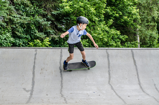 Young boy going up on ramp with skateboard seen from side during day of summer