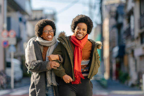 Black twin sisters walking in street arm in arm happily Black twin sisters are walking in the street arm in arm happily. arm in arm stock pictures, royalty-free photos & images