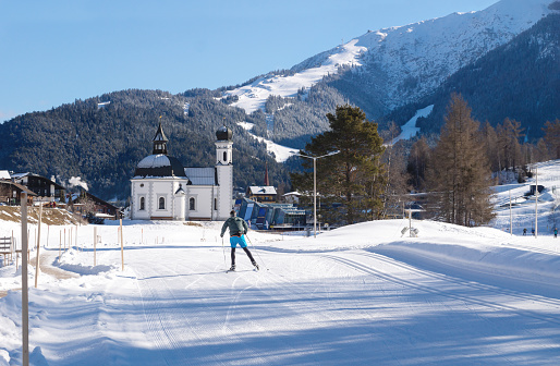 Seefeld, Tirol, Austria - 8 March 2020: Cross-country skier on sunny track towards typical Austrian picturesque church