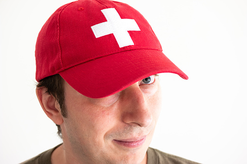 Adult Caucasian male head shot wearing red baseball hat with Swiss national symbol close 2020