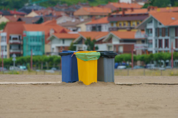 Street trash bins for separate garbage collection. Blue, yellow and gray waste bins. European small town citysape as background. Photography at the sandy beach.