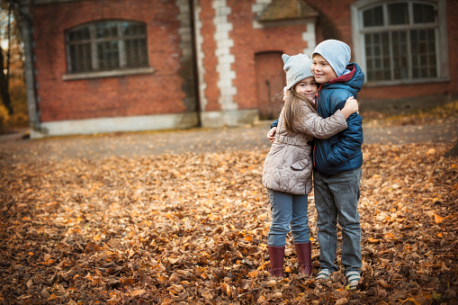 The girl hugs the boy tightly on an autumn day near an old red brick house.