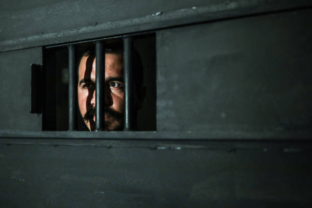 istock Young Man Behind Bars in Prison 1256338673