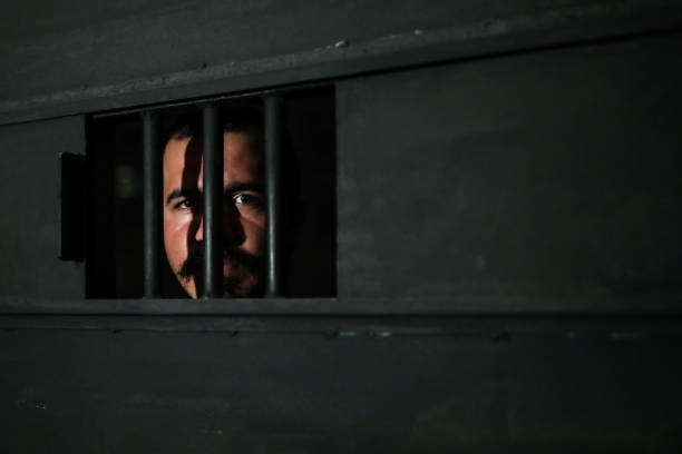 istock Young Man Behind Bars in Prison 1256339307