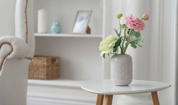 розовые и желтые розы в современной белой вазе на белом столе рядом с классическим креслом - side table стоковые фото и изображения