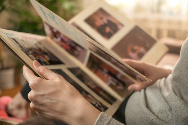 ragazza con una giacca grigia è seduta sul divano e guardando vecchie foto in un album fotografico - ricordi foto e immagini stock