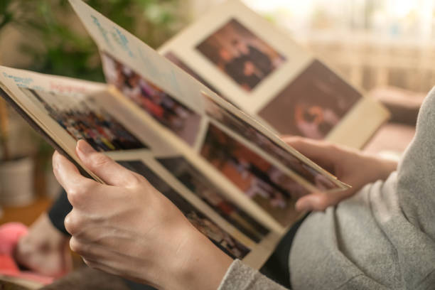 girl in a gray jacket is sitting on the sofa and looking at old photos in a photo album girl in a gray jacket is sitting on the sofa and looking at old photos in a photo album east slavs photos stock pictures, royalty-free photos & images