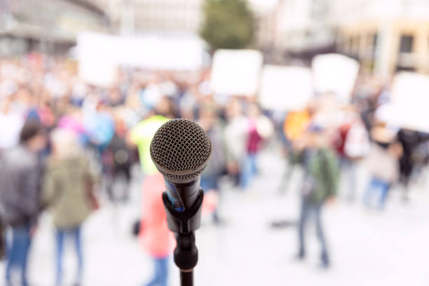 istock Public demonstration or political protest. Microphone in focus against unrecognizable crowd of people. 1256346757