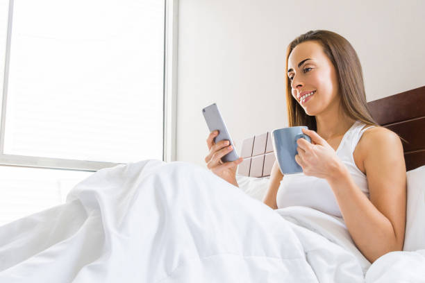 istock Woman in bed checking her cell phone first thing in the morning while drinking coffee 1256347025