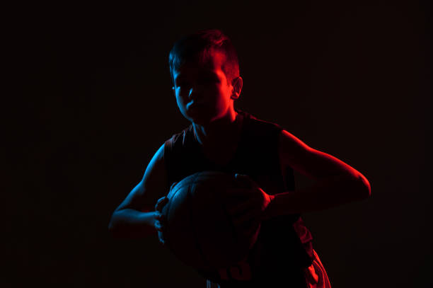 istock Boy Holding Basketball While Standing Against Black Background 1256347195