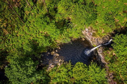 A high angle view captured by a drone flying above a waterfall  in a forest in Scotland. The forest is in a remote rural area of Dumfries and Galloway in the south west of Scotland.
During the summer the waterfall is hidden from a nearby footpath by the leaves on the surrounding trees.