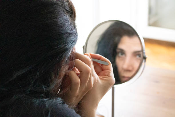 istock A young woman tweezing her eyebrows in front of a mirror 1256349937