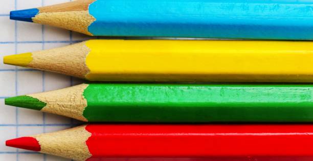 istock Four colored pencils on a notebook sheet in a cage. To close. 1256351115