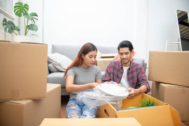 istock Young Asian couple packing their belonging into cardboard box by using a check list before moving to new resident or house after buy or rent a new one. 1256351300