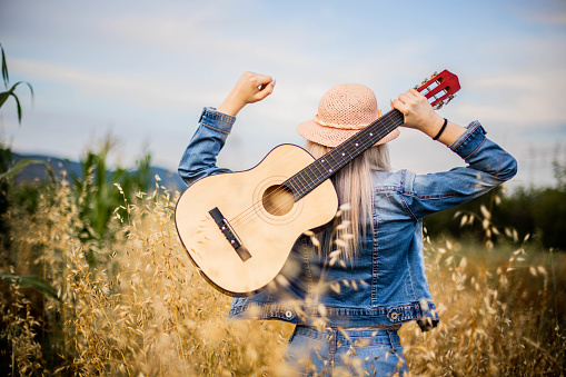 Blonde women enjoying  at field. Young beautiful women is playing guitar at field. Women is walking trought the field.