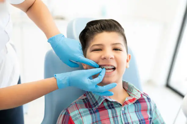 Female orthodontist examining cute boy wearing braces