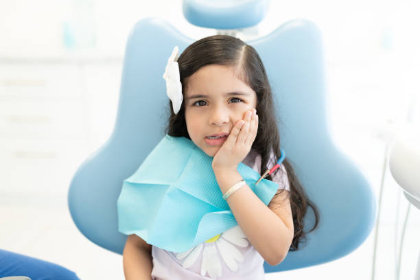 Latin Girl Visiting Dentist For Checkup Portrait of cute little girl suffering from toothache sitting on chair at dental clinic toothache stock pictures, royalty-free photos & images