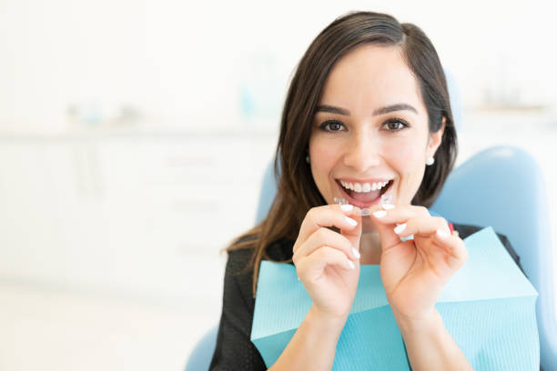 Attractive Woman Holding Invisible Aligner Happy mid adult woman with clear orthodontic retainer in dental clinic dental aligner photos stock pictures, royalty-free photos & images