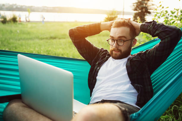 istock Angry young hipster businessman having serious video conversation while sitting in park in hammock at sunset 1256362557