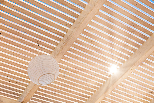 Sun shining trough a wooden timber pergola roof creating a sunbeam, star shaped light