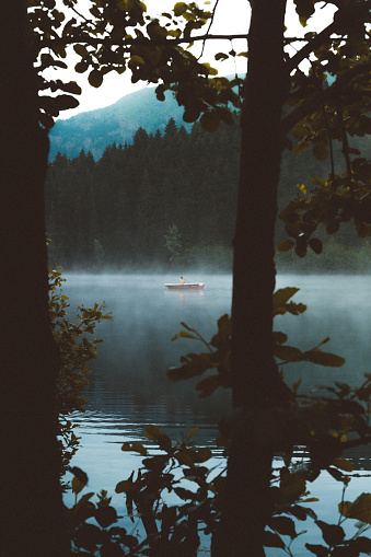 Beautiful scenery landscape young man in yellow jacket on red small boat enjoying  a misty early morning paddling haze over the Karagöl lake surrounded with forest on sunrise in Şavşat, Artvin, Turkey