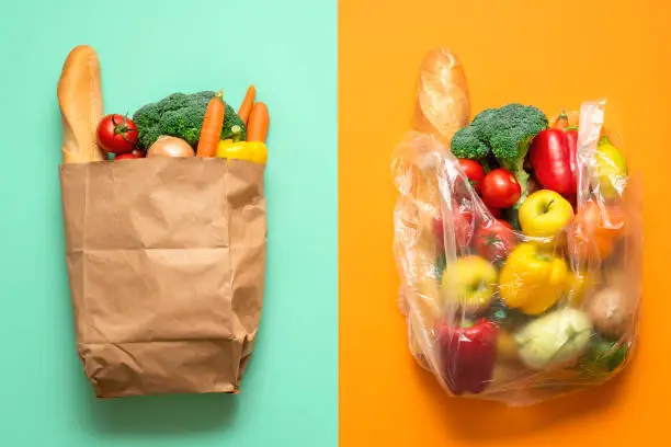 Top view with groceries in plastic and paper bags on a bicolored background. Concept for plastic-free shopping. Choosing between paper and plastic bags.