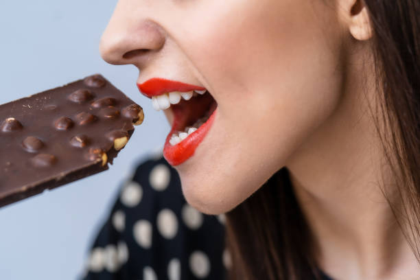 istock Young attractive woman eats chocolate. Close up. Black chocolate with nuts. 1256370077