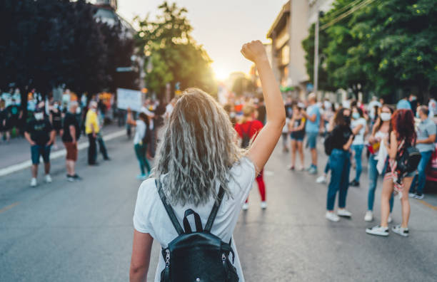 Young woman protester raising her fist up Young woman with a raised fist protesting in the street strength photos stock pictures, royalty-free photos & images