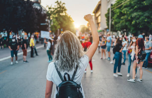 Young woman protester raising her fist up Young woman with a raised fist protesting in the street campaigner stock pictures, royalty-free photos & images