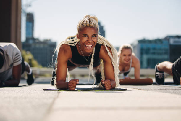 Group of people doing core exercise Group of young adults working out together outside in the city. Men and women holding a plank position and smiling. bodyweight training stock pictures, royalty-free photos & images