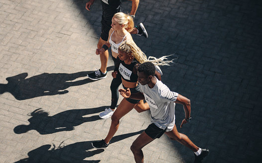 Multi-ethnic group of people running together. High angle view of running club members exercising together in the city.