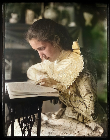 Colourised historical photo of a young Victorian girl reading a book