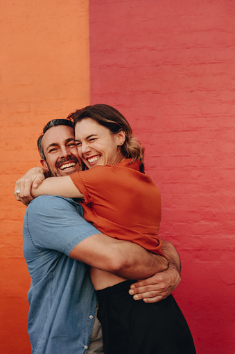 Loving middle aged couple embracing against colored wall. Mature man and woman together against red and orange wall.