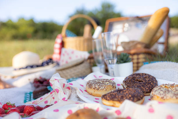 Picnic in nature in summer. Picnic basket with baguette, champagne, fruit, and doughnuts