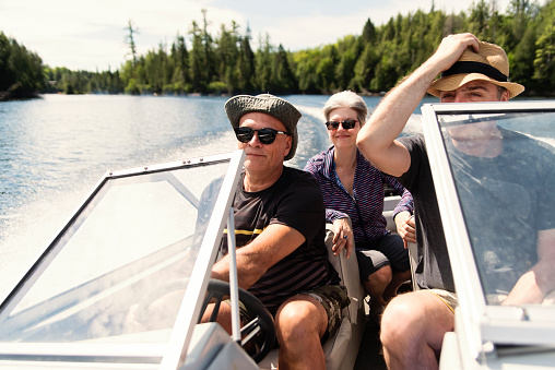 50+ friends enjoying vacations and a sunny day on a small boat on a lake. They are wearing casual clothes and sunglasses. The two men are brothers-in-law. Horizontal waist up outdoors shot with copy space.