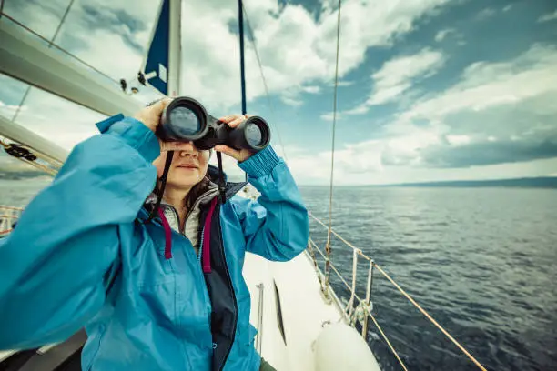 A woman on the sailing yacht looking through binoculars
