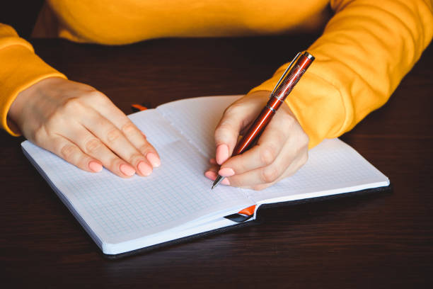 istock Young woman holds a pen in her left hand and writes  note in blank notebook. International Left-Handers Day 1256382109