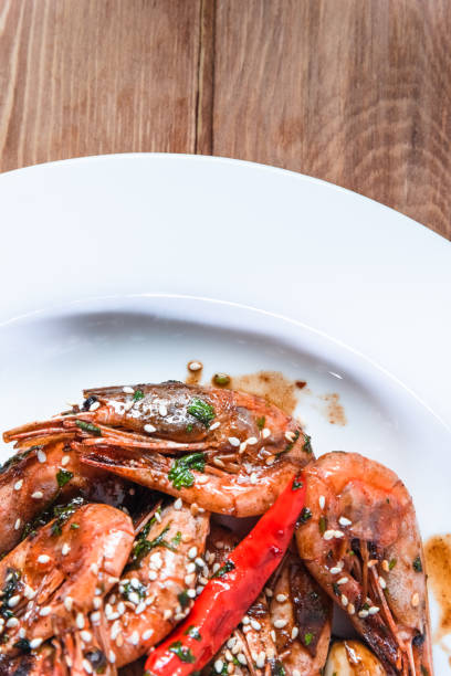 istock Appetizing fried shrimp with specialties, sesame seeds and lemon, on a white plate on a background of wood. Food concept in restaurants and bars 1256382123