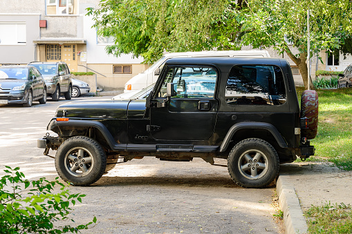 Varna, Bulgaria, July 11, 2020. Side view of two door black jeep wrangler parked on an outdoor parking lot near multi-storey apartment building on a sunny summer day.