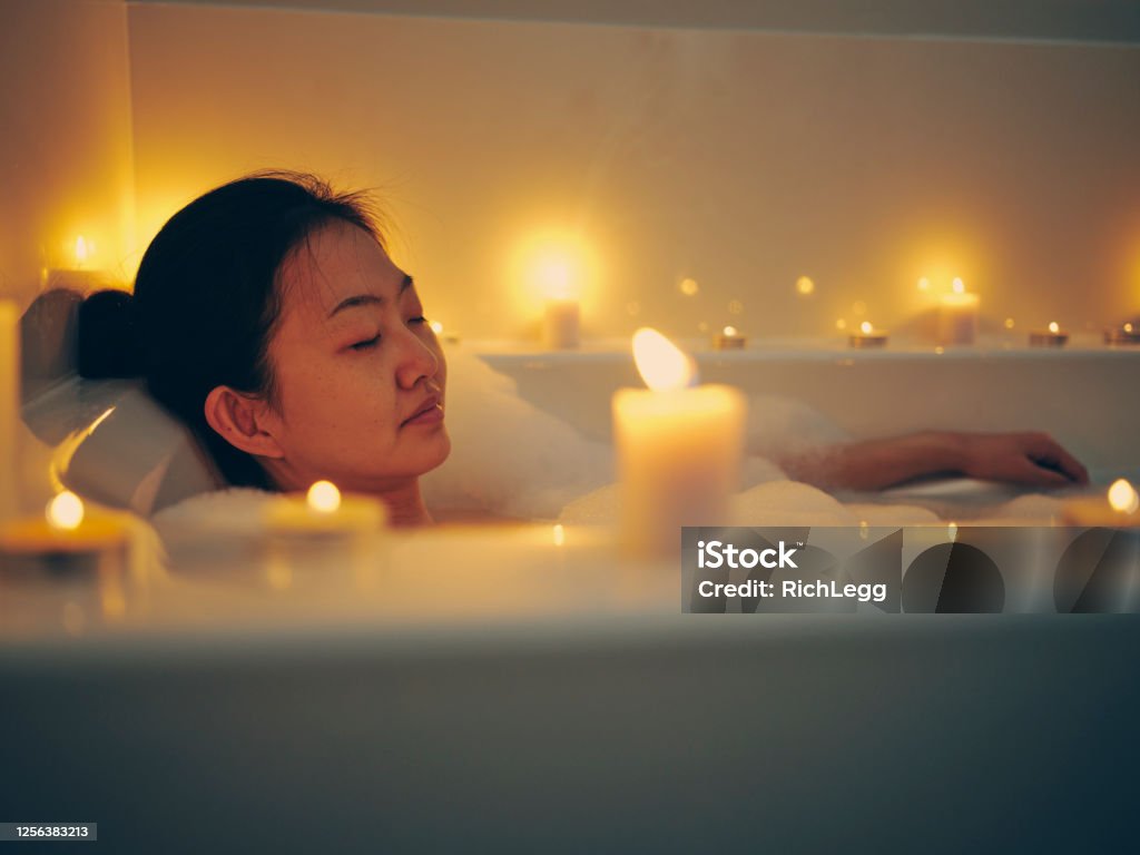 Japanese Woman Taking a Candlelight Bath A young Japanese woman relaxing in a bathtub, surrounded by candles. Bathtub Stock Photo