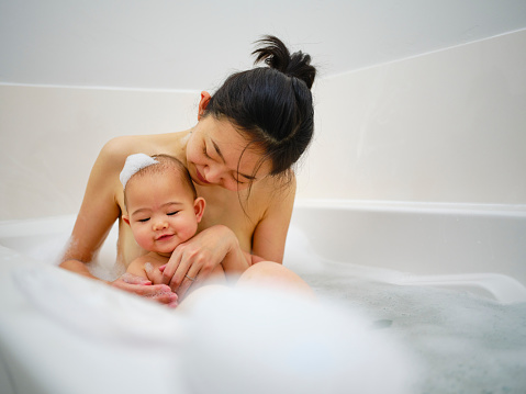 A young Japanese mother relaxing in a bathtub with her infant daughter.
